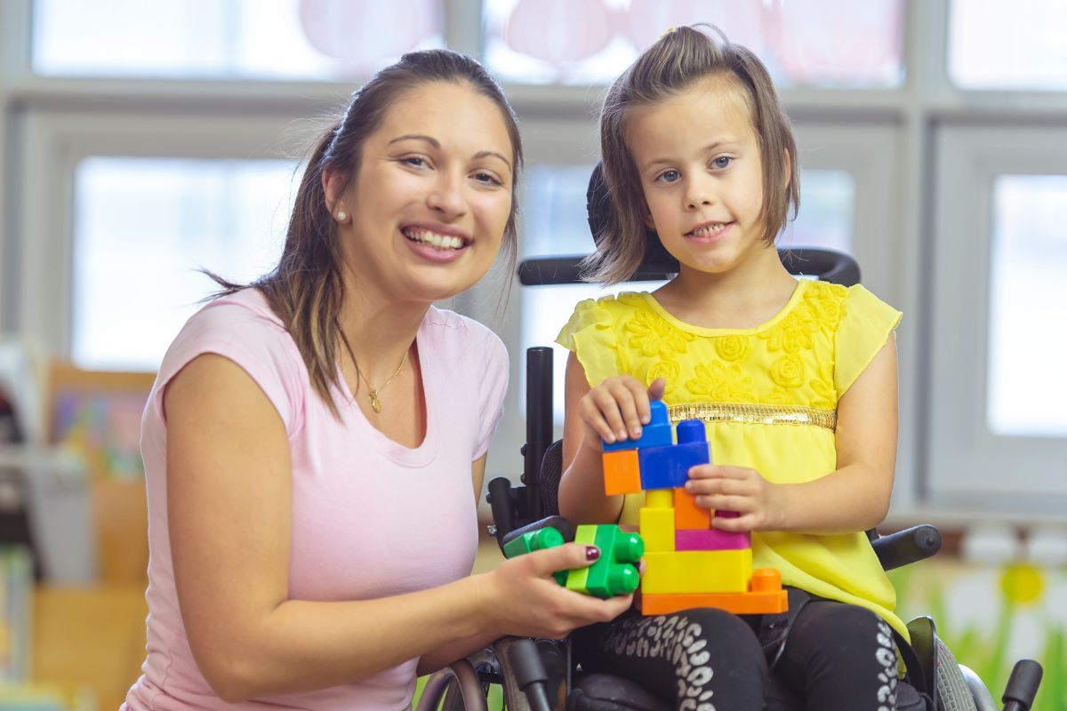 Smiling carer with a young girl using a wheelchair, holding colourful building blocks