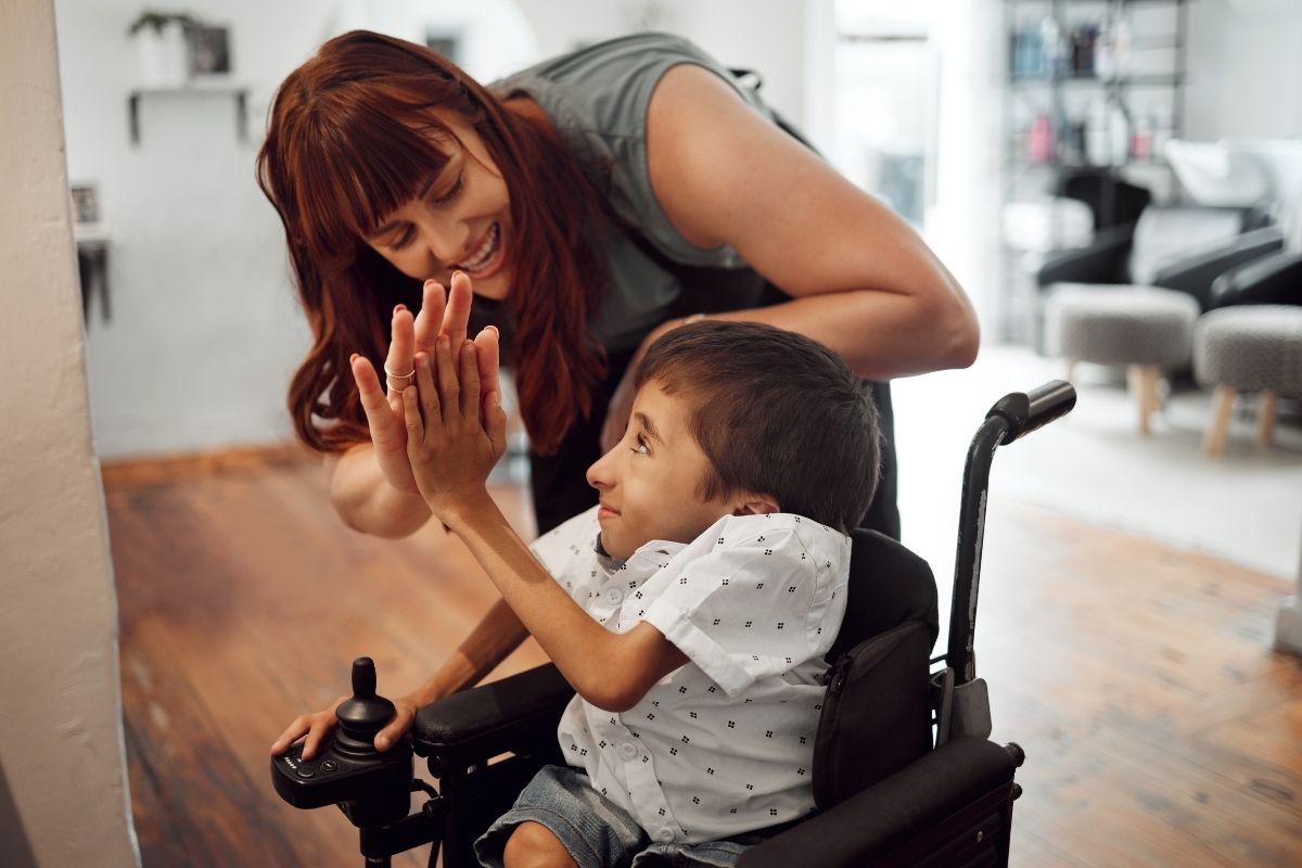 Carer high-fiving a child using a powered wheelchair at home