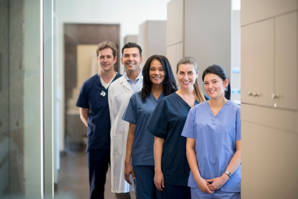 Group of healthcare staff in scrubs standing in a clinic hallway, smiling at the camera