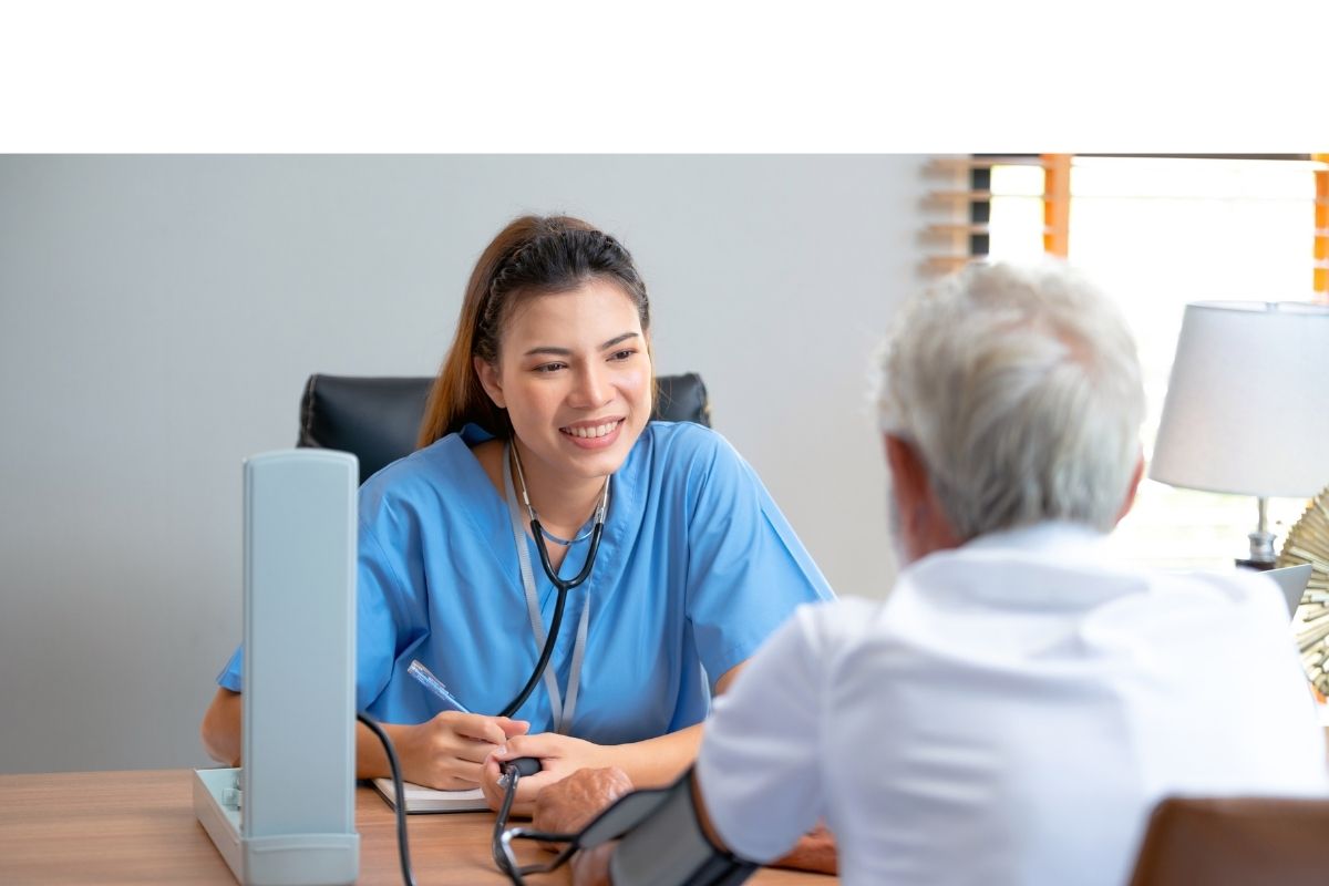 Nurse in blue scrubs checking an older adult’s blood pressure during a home visit