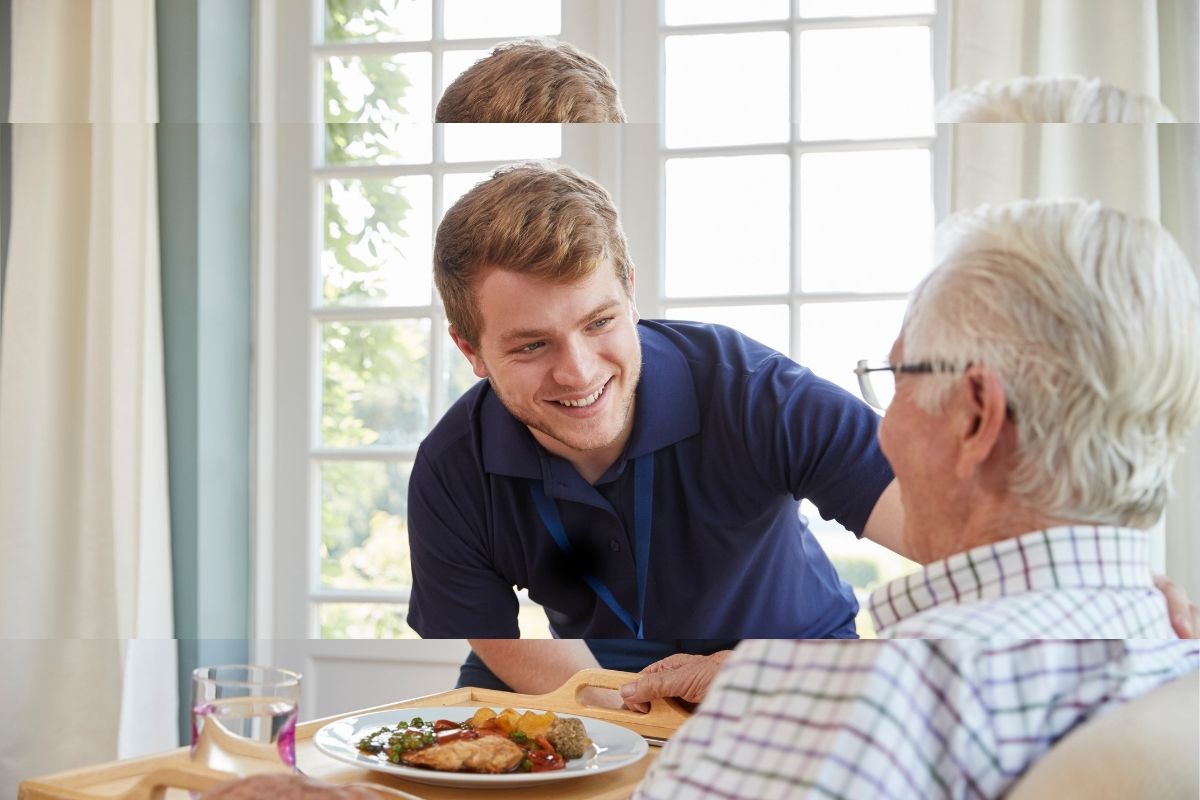 Support worker smiling while serving lunch to an older man at home